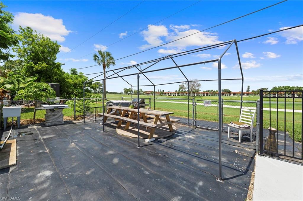 Outdoor patio space featuring a metal frame structure, black ground covering, and chain-link fencing