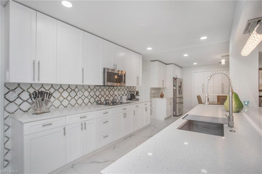 White shaker cabinetry, patterned tile backsplash, stainless steel appliances, solid surface countertops, and recessed lighting