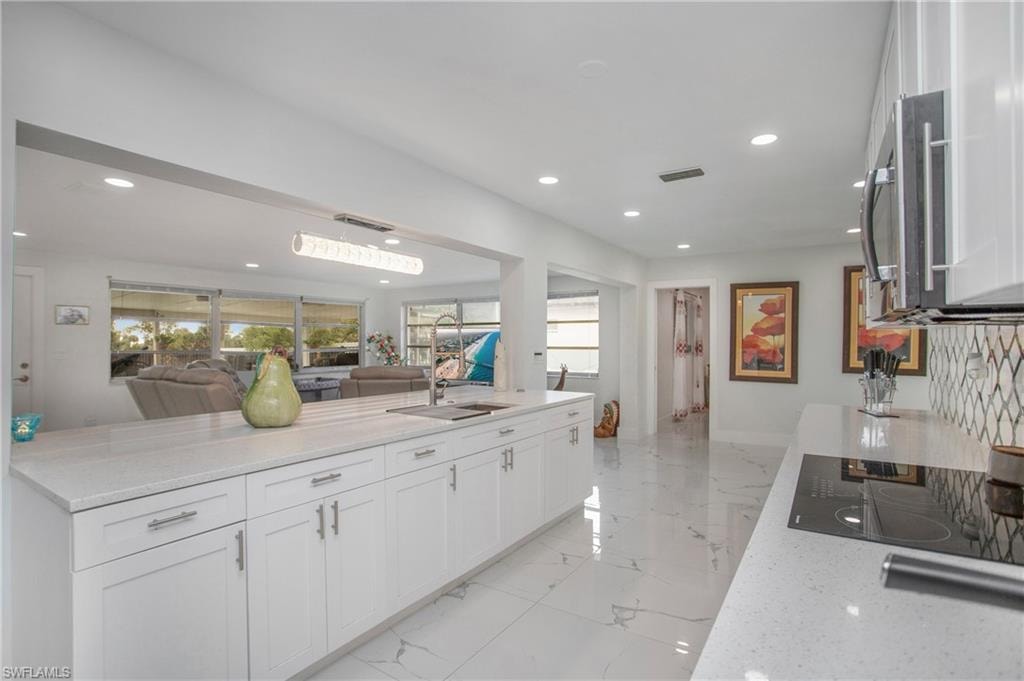 Modern kitchen featuring white cabinetry, light-toned countertops, a built-in cooktop, and a stainless steel microwave