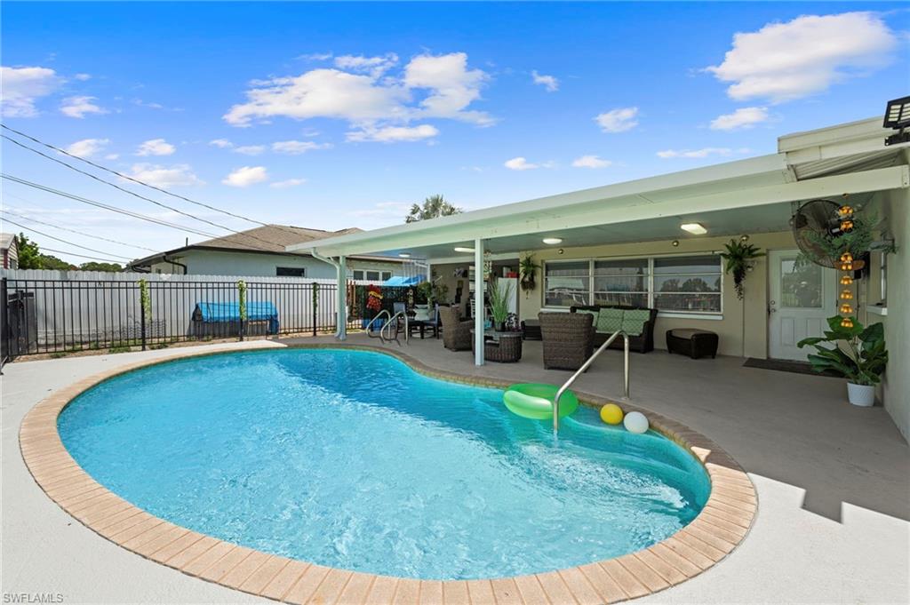 Curved swimming pool with brick coping, metal fencing, and an expansive covered patio with recessed lighting