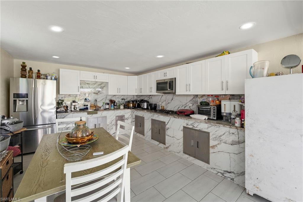 White shaker cabinetry, marble-patterned backsplash and countertops, recessed lighting, and tile flooring
