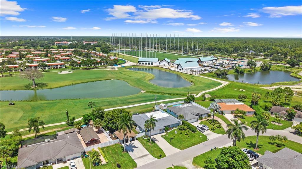 Aerial perspective showcasing residential properties, a golf course with water features, and a golf driving range facility