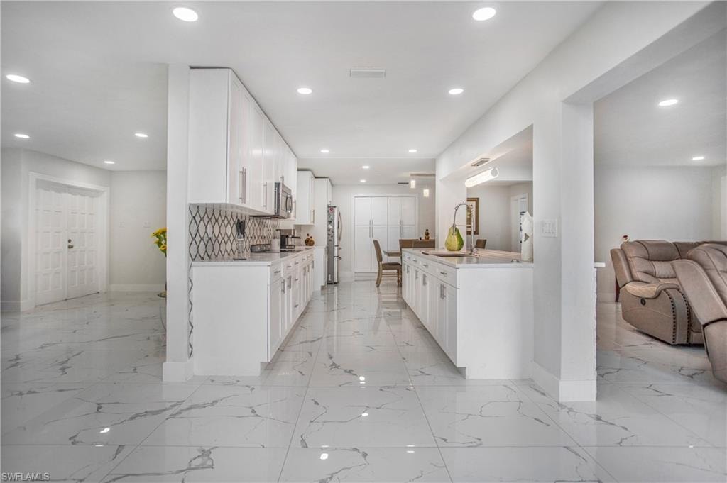 Modern kitchen featuring white cabinetry, stainless steel appliances, a patterned backsplash, and marbled floor tile