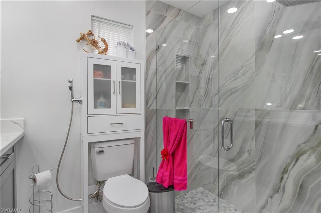 Glass-enclosed shower with marbled tile surround, built-in shower niche, and pebbled floor