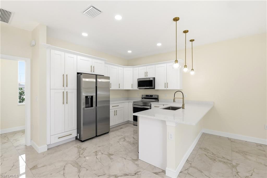Kitchen featuring white cabinetry, stainless steel appliances, a center island with sink, pendant lighting, and large format floor tiles