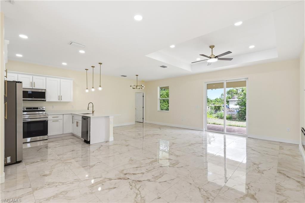 Open-concept living space with large format tile flooring, a kitchen island with pendant lighting, white cabinetry, and stainless steel appliances