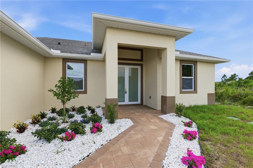 Stucco exterior with contrasting trim, paver walkway, double front entry doors, and a landscaped garden bed with decorative white stone
