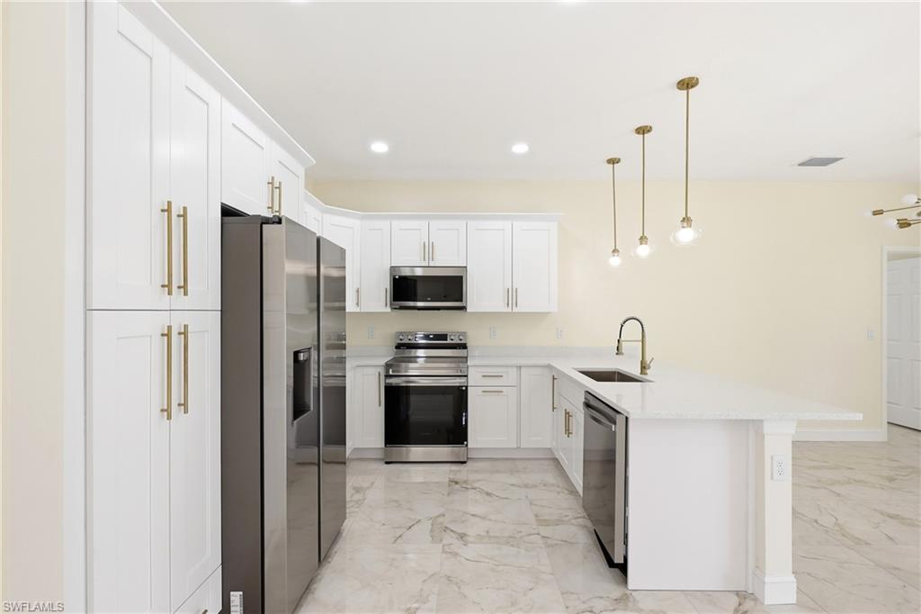 Modern kitchen featuring white cabinetry, stainless steel appliances, a white stone countertop island, and marble-look tile flooring