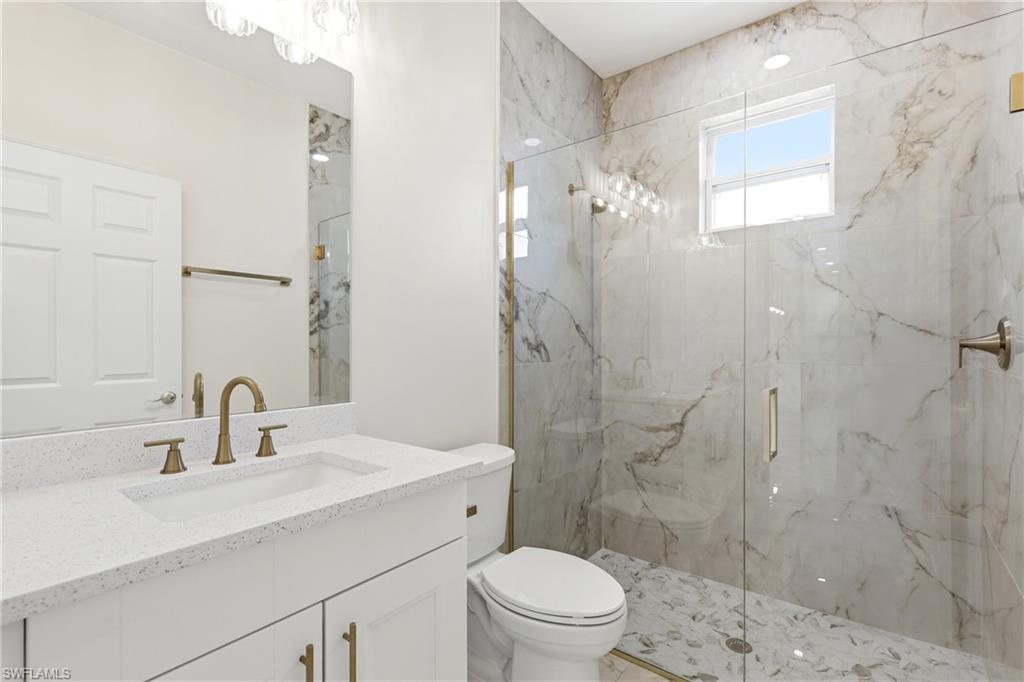 White vanity with quartz countertop, undermount sink, and brass-finish fixtures