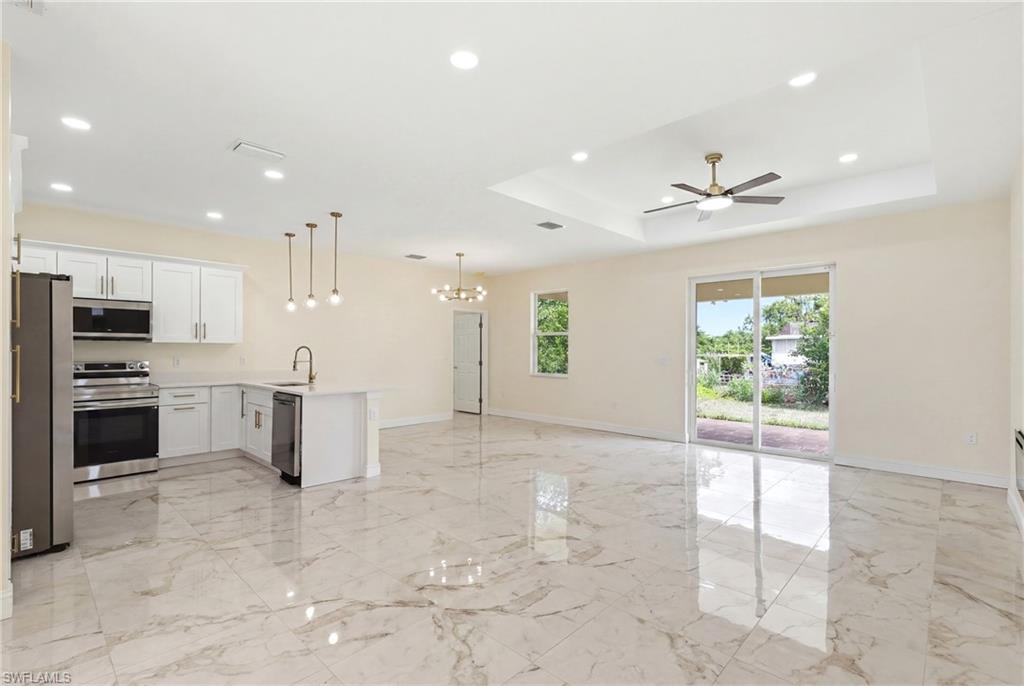Spacious open-concept living area featuring polished stone flooring throughout, recessed and pendant lighting, a ceiling fan, and sliding glass doors providing natural light