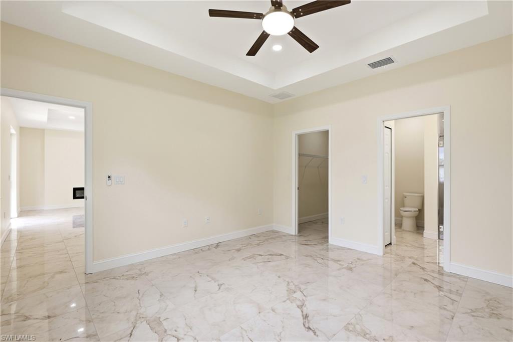 Tray ceiling with a ceiling fan, marble-look tile flooring, and light-colored walls