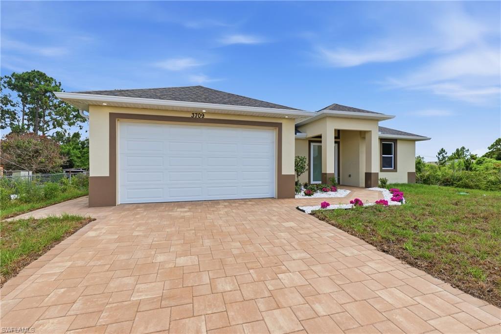Property exterior featuring a paver driveway, an attached garage, a covered entry, decorative landscaping, and a pitched roof