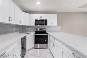 Kitchen featuring white cabinetry, appliances with stainless steel finishes, light marble finish floors, recessed lighting, and backsplash
