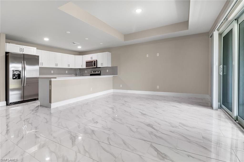 Kitchen featuring stainless steel appliances, open floor plan, a raised ceiling, light countertops, and white cabinetry