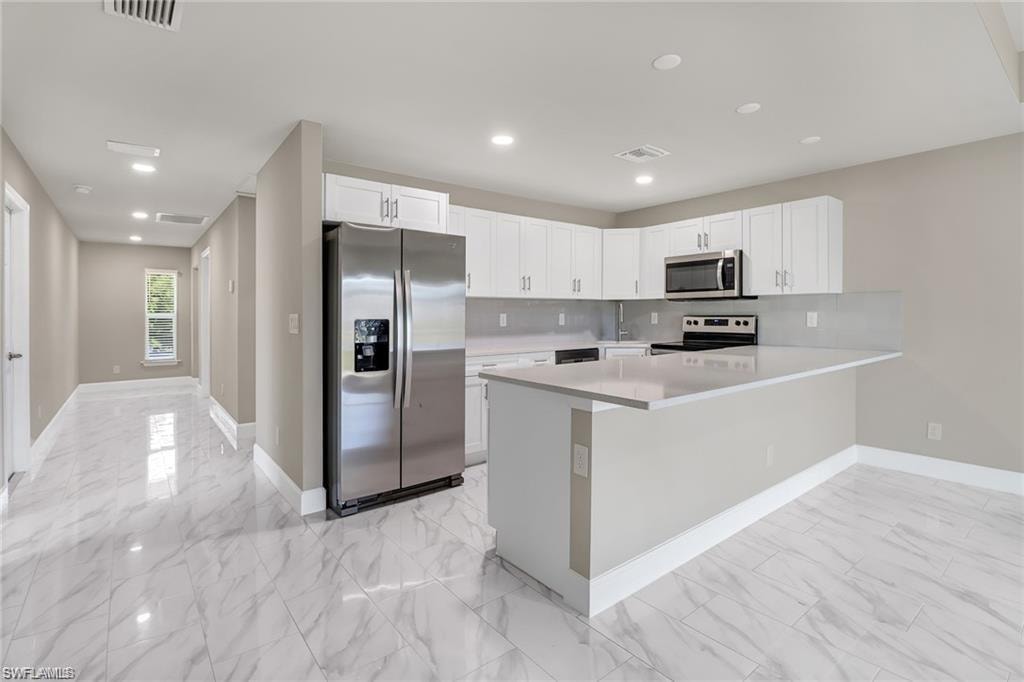 Kitchen with appliances with stainless steel finishes, white cabinetry, tasteful backsplash, a peninsula, and recessed lighting
