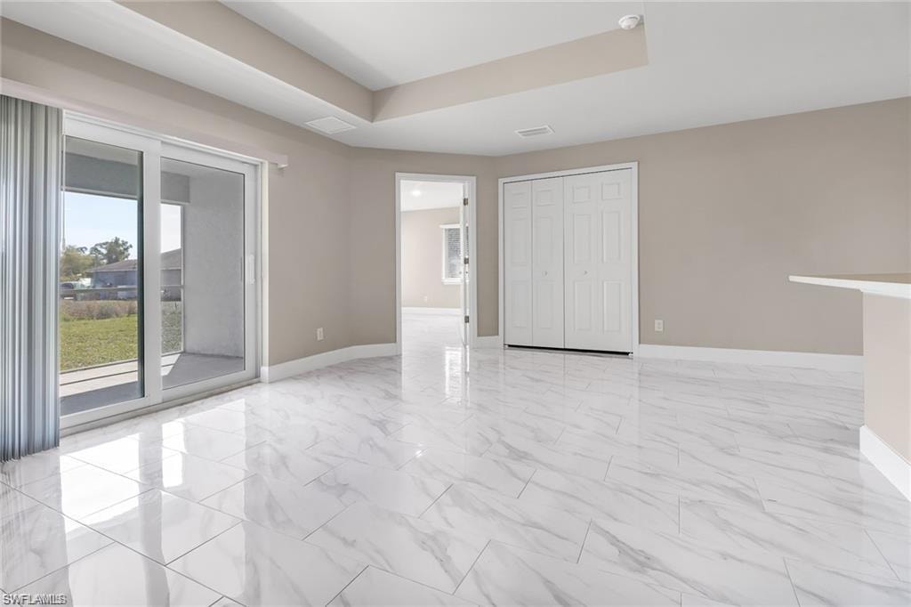 Unfurnished bedroom featuring light marble finish floors, access to outside, a closet, and a tray ceiling