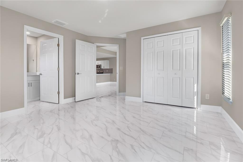 Unfurnished bedroom featuring light marble finish flooring, a closet, and ensuite bath