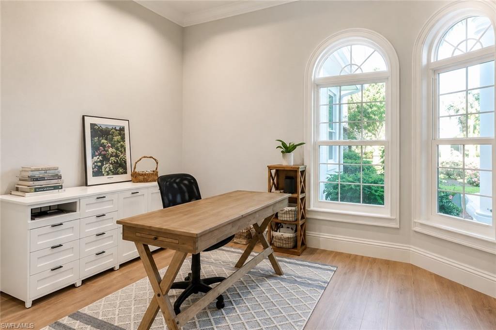 Light wood-finish flooring with white baseboards, two arched windows with grid panes, and built-in white cabinetry with dark pulls
