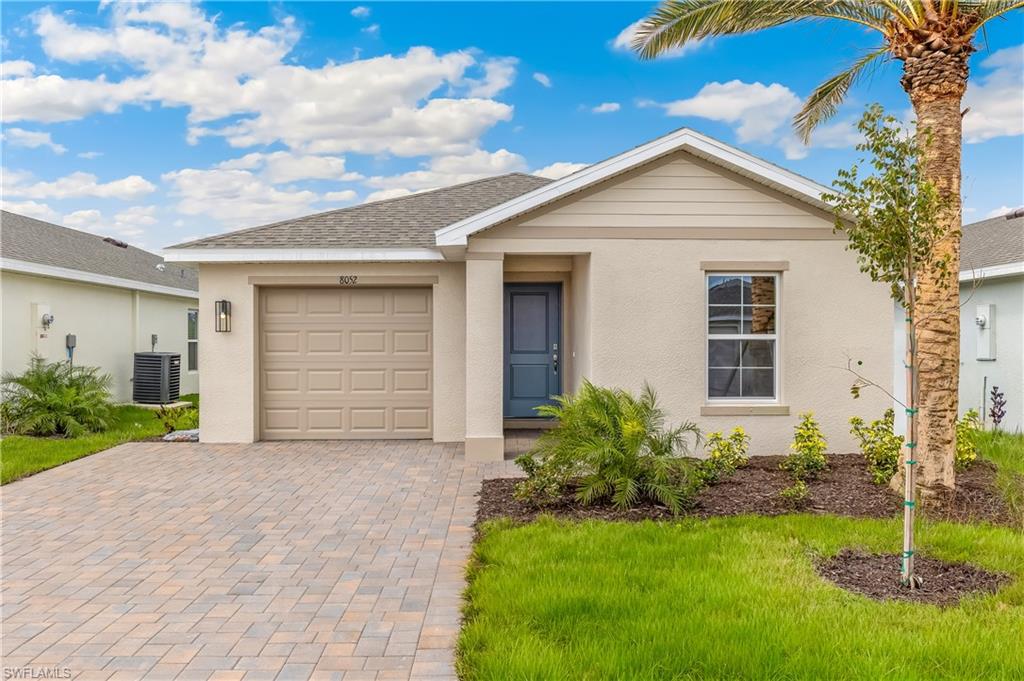 Stucco exterior, single-car garage, paver driveway, well-maintained lawn, and a prominent palm tree