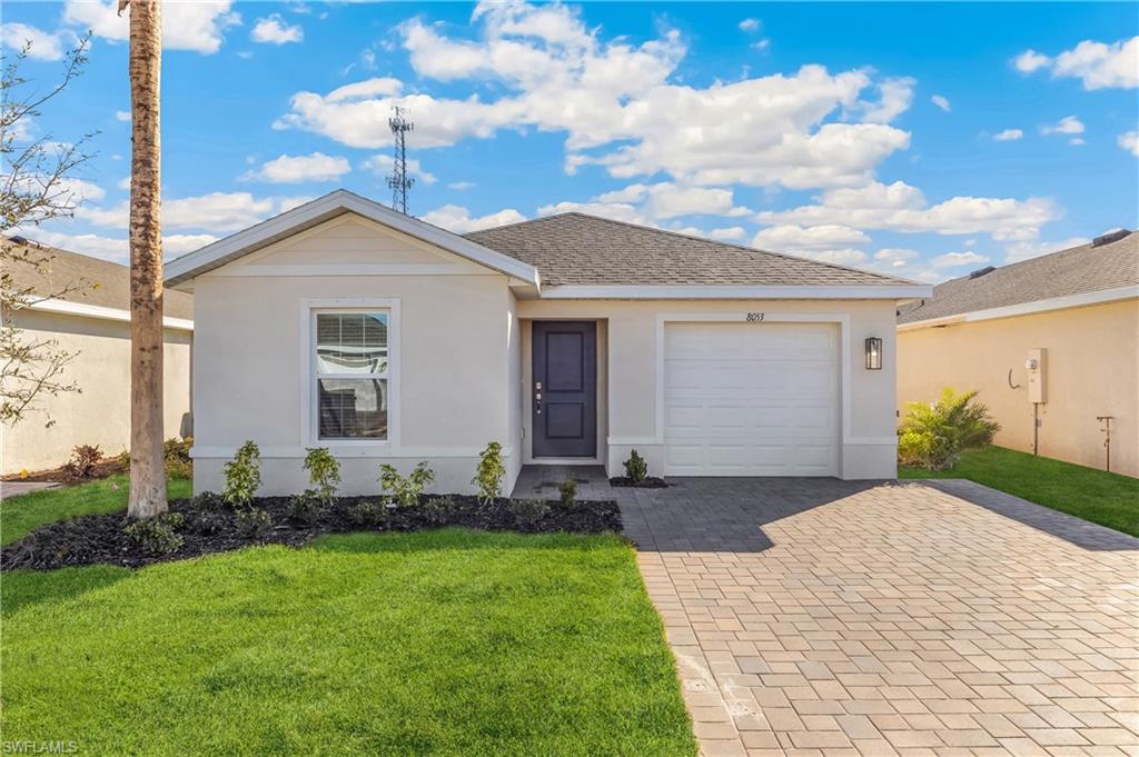 Stucco exterior, paver driveway, attached single-car garage, dark entry door, and manicured landscaping