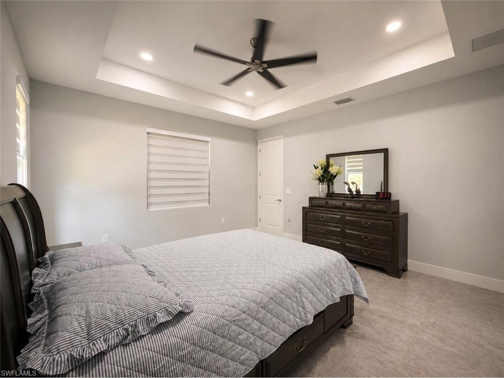 Tray ceiling with recessed lighting, ceiling fan, window with horizontal blinds, light gray wall finish, and neutral-toned floor tile