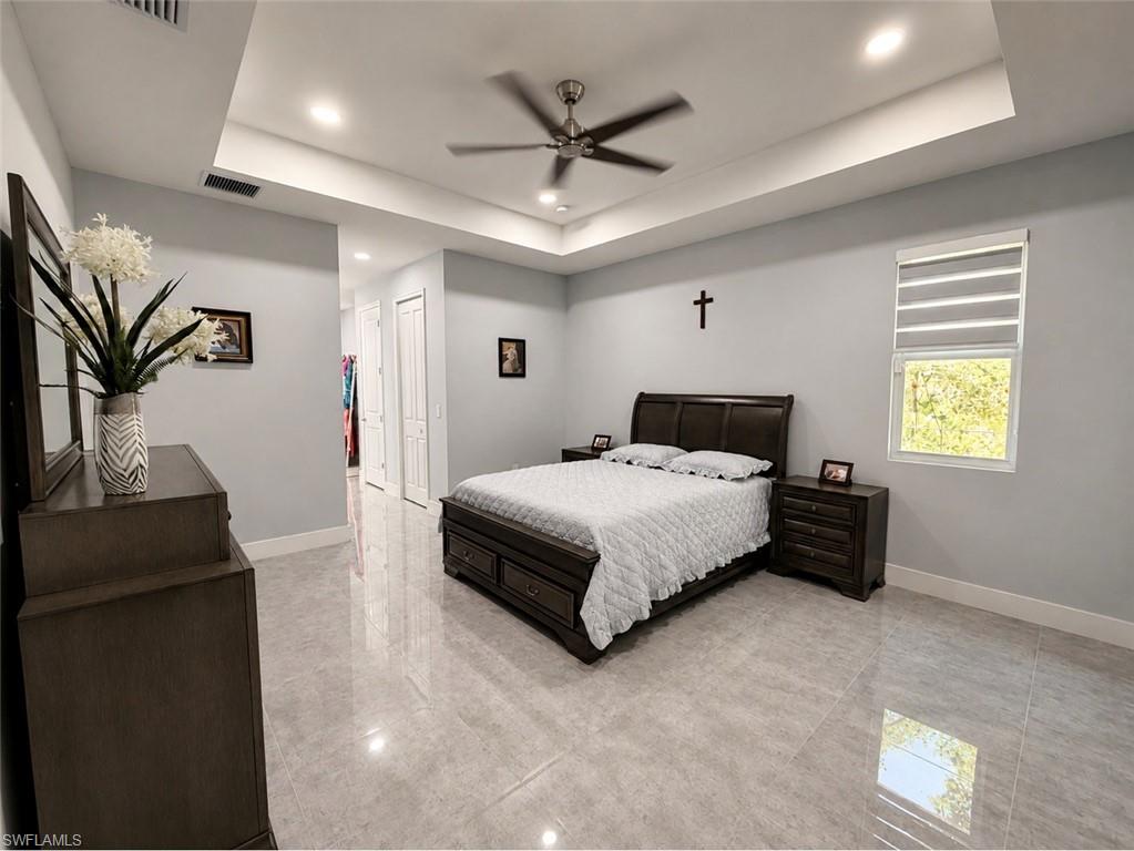 Tray ceiling with recessed lighting and a ceiling fan, large window with horizontal blinds, light gray wall color, and polished tile flooring