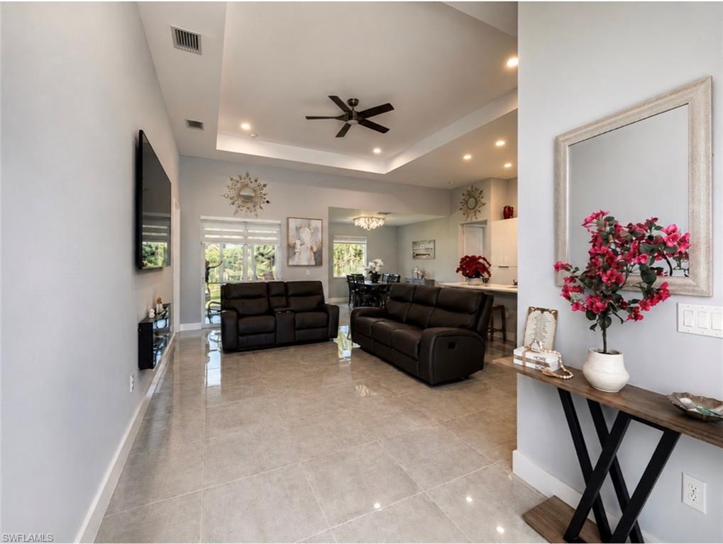 Spacious living area featuring large format tile flooring, a tray ceiling with recessed lighting, and a ceiling fan