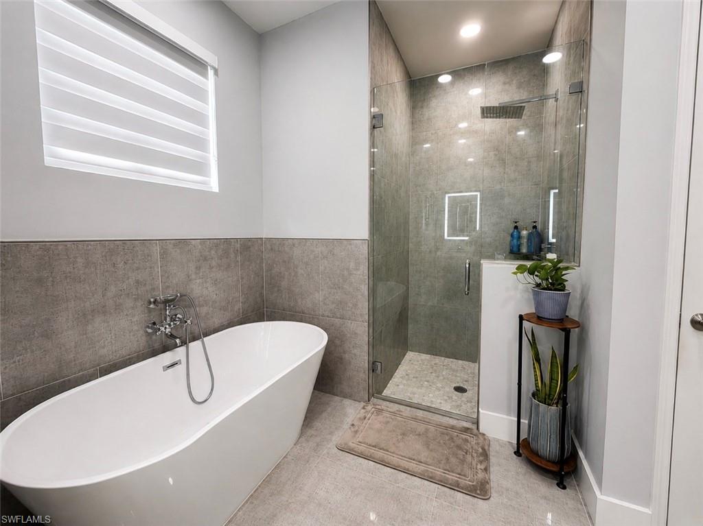 Freestanding soaking tub with wall-mounted chrome fixtures, glass-enclosed shower with rain showerhead, and tiled walls and flooring