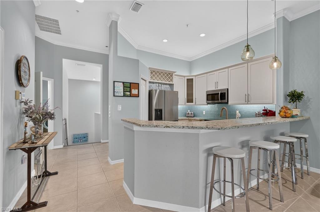 Kitchen featuring white cabinetry, stainless steel appliances, a tile backsplash, and a breakfast bar with quartz  countertops