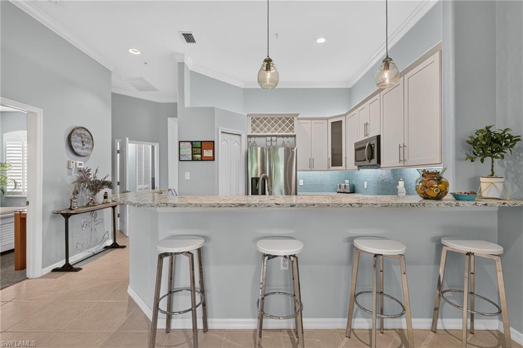 Kitchen featuring a breakfast bar with stone countertop, stainless steel appliances, custom cabinetry, and pendant lighting