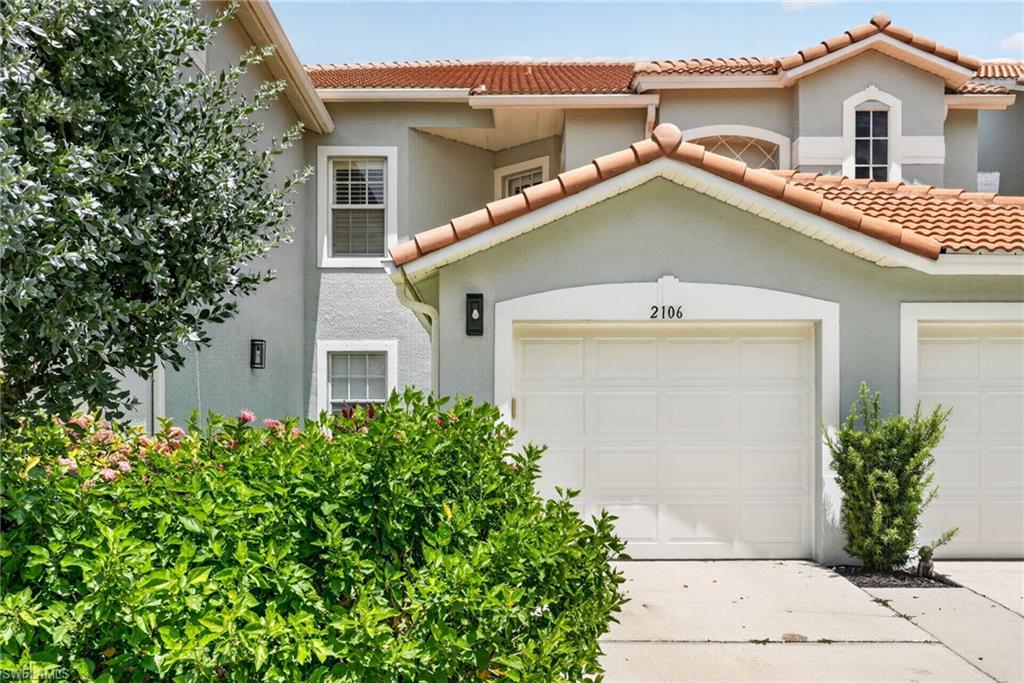 Stucco exterior with a terra cotta tile roof, multiple windows, and a panel garage door.