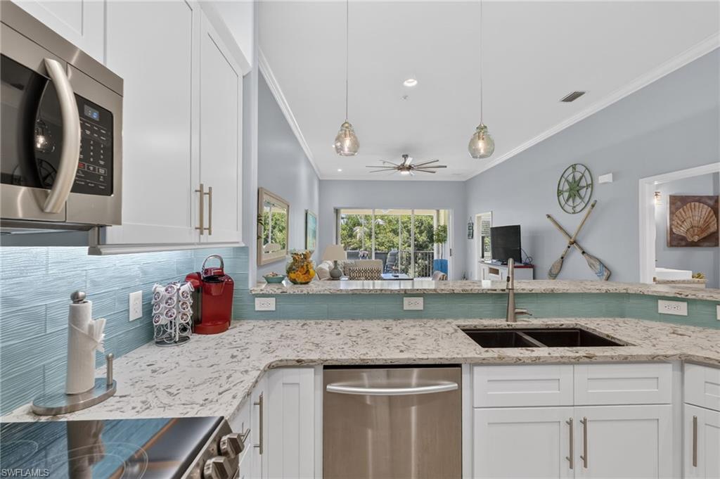 Kitchen featuring white shaker cabinetry, stainless steel appliances, light-toned countertops, a blue tiled backsplash, and dual pendant lighting.