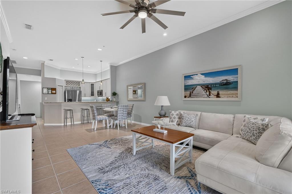 Open-concept living space with tile flooring, a ceiling fan, and crown molding.