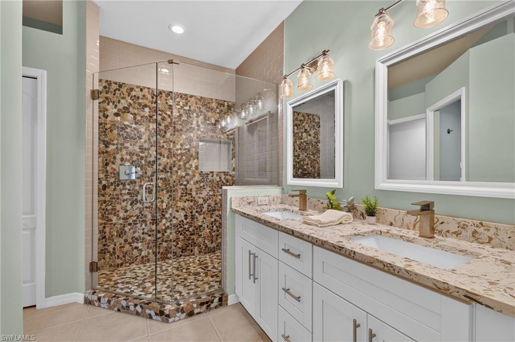 Spacious bathroom featuring a frameless glass shower enclosure, river rock tile accents, dual vanities with integrated sinks, and individual framed mirrors.