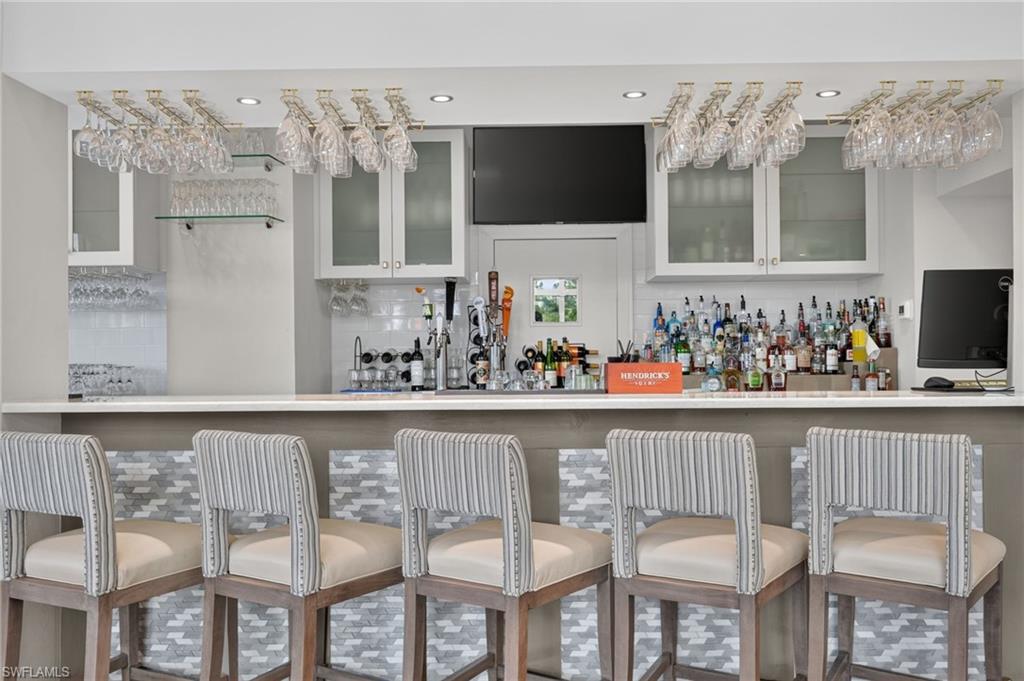 Wet bar with overhead stemware storage, under-cabinet lighting, built-in display cabinetry, and a television