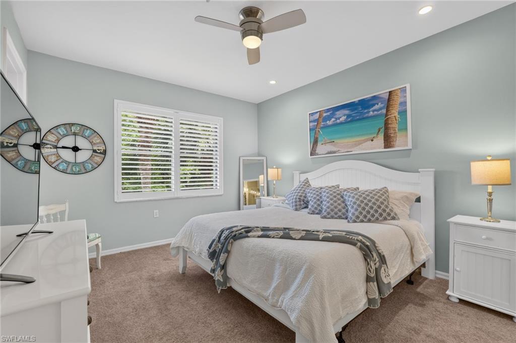 Carpeted bedroom featuring a ceiling fan with integrated lighting, recessed lighting, and a window with plantation shutters.
