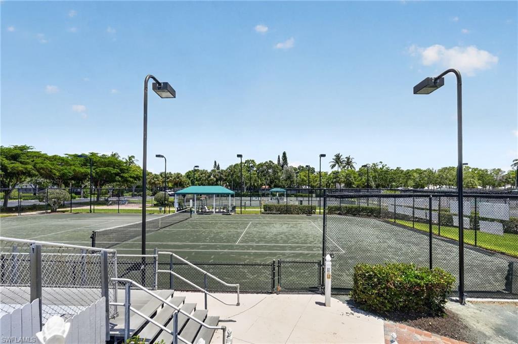 Multiple tennis courts with chain-link fencing, featuring overhead lighting fixtures and a covered gazebo.