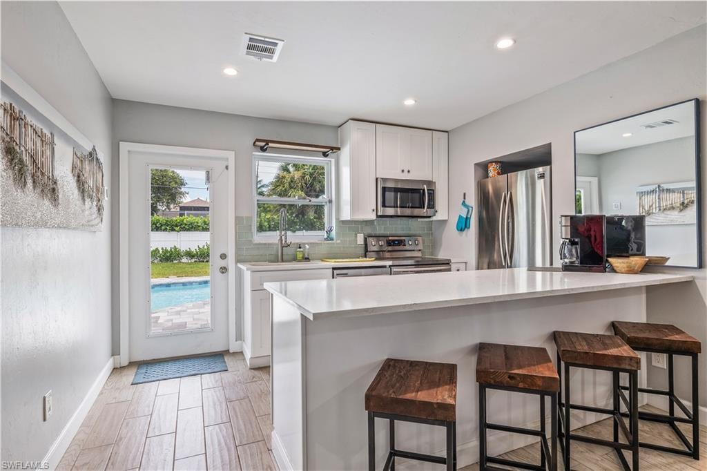 Kitchen with appliances with stainless steel finishes, a kitchen breakfast bar, sink, tasteful backsplash, and white cabinetry