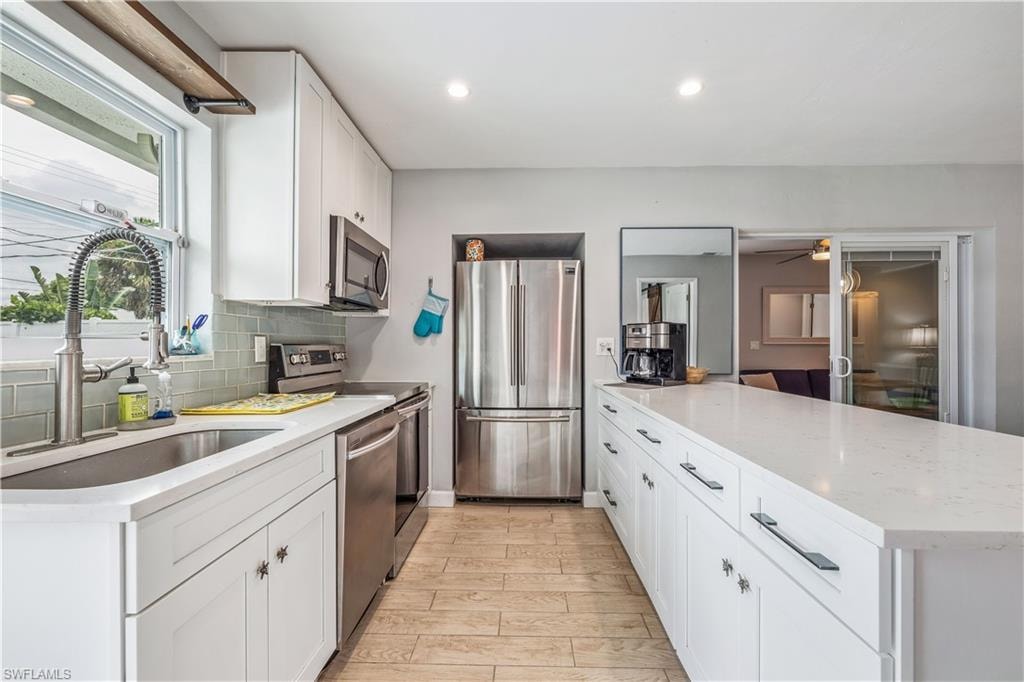 Kitchen with appliances with stainless steel finishes, white cabinets, light stone countertops, backsplash, and sink