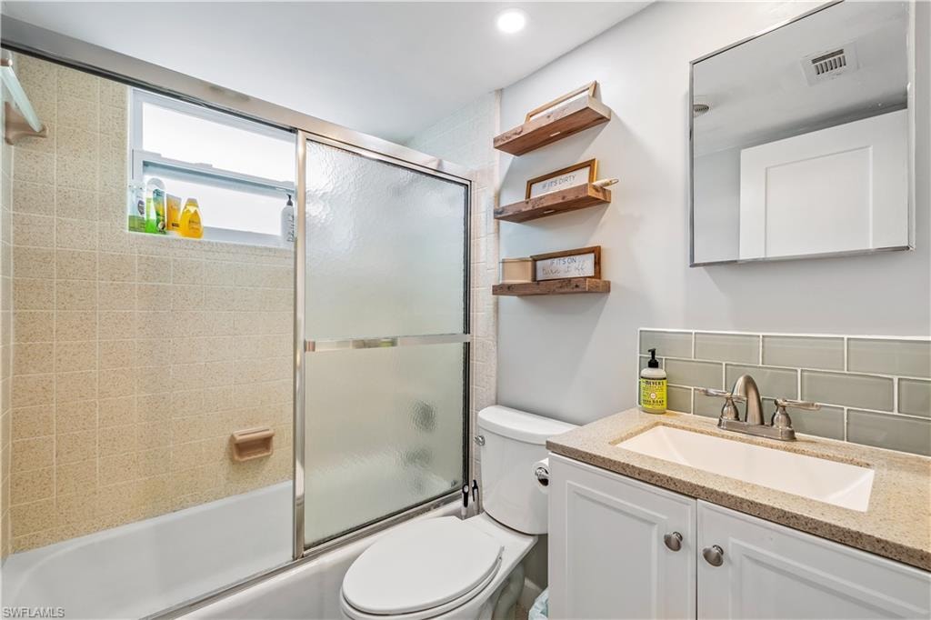 Full bathroom featuring tasteful backsplash, vanity, toilet, and shower / bath combination with glass door