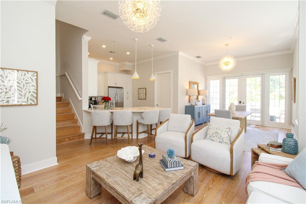 Living room featuring light wood-style flooring, stairs, visible vents, and a notable chandelier