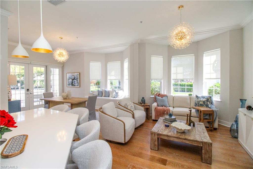 Living area with visible vents, french doors, ornamental molding, light wood-type flooring, and an inviting chandelier