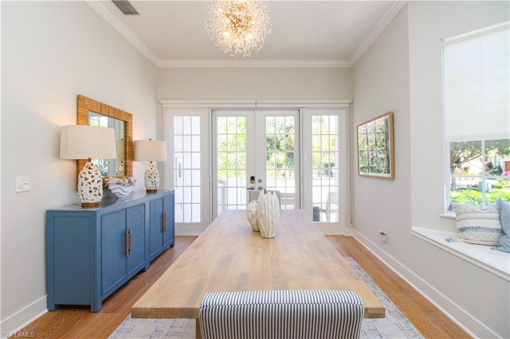 Dining area featuring light wood finished floors, visible vents, ornamental molding, an inviting chandelier, and french doors