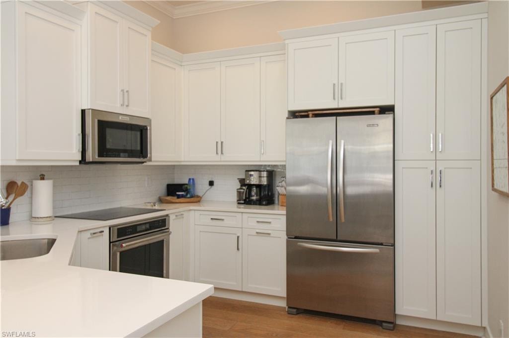 Kitchen featuring stainless steel appliances, white cabinets, light countertops, ornamental molding, and tasteful backsplash