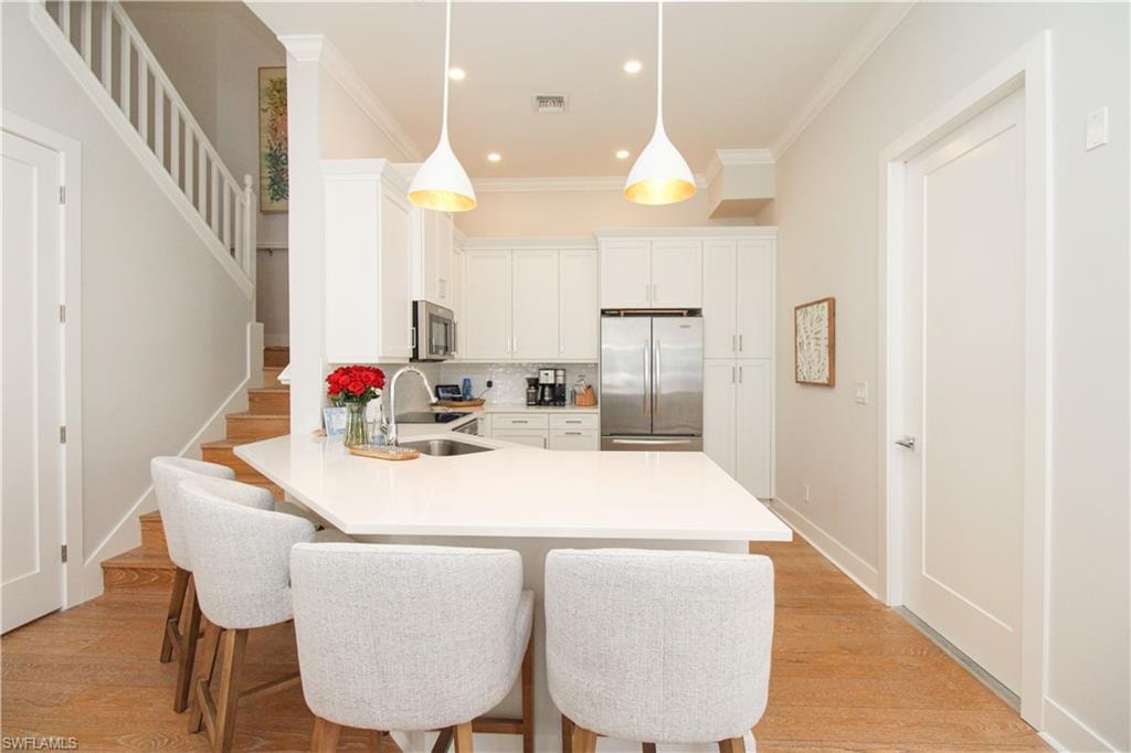 Kitchen with a sink, white cabinetry, light countertops, appliances with stainless steel finishes, and pendant lighting