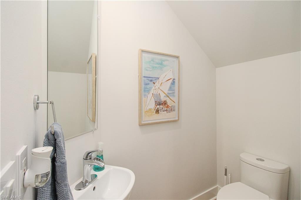 Half bathroom with toilet, baseboards, vaulted ceiling, and a sink
