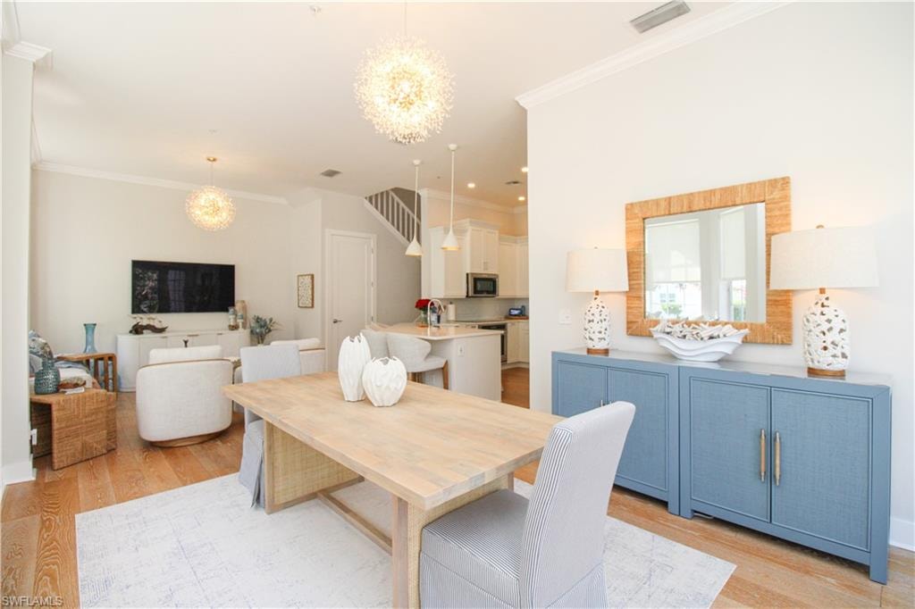 Dining space with light wood-style flooring, visible vents, a chandelier, and crown molding