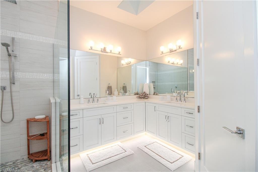 Full bath featuring double vanity, a skylight, a tile shower, and a sink