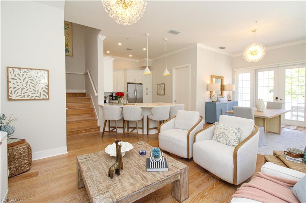 Living room with stairs, light wood finished floors, crown molding, and a notable chandelier