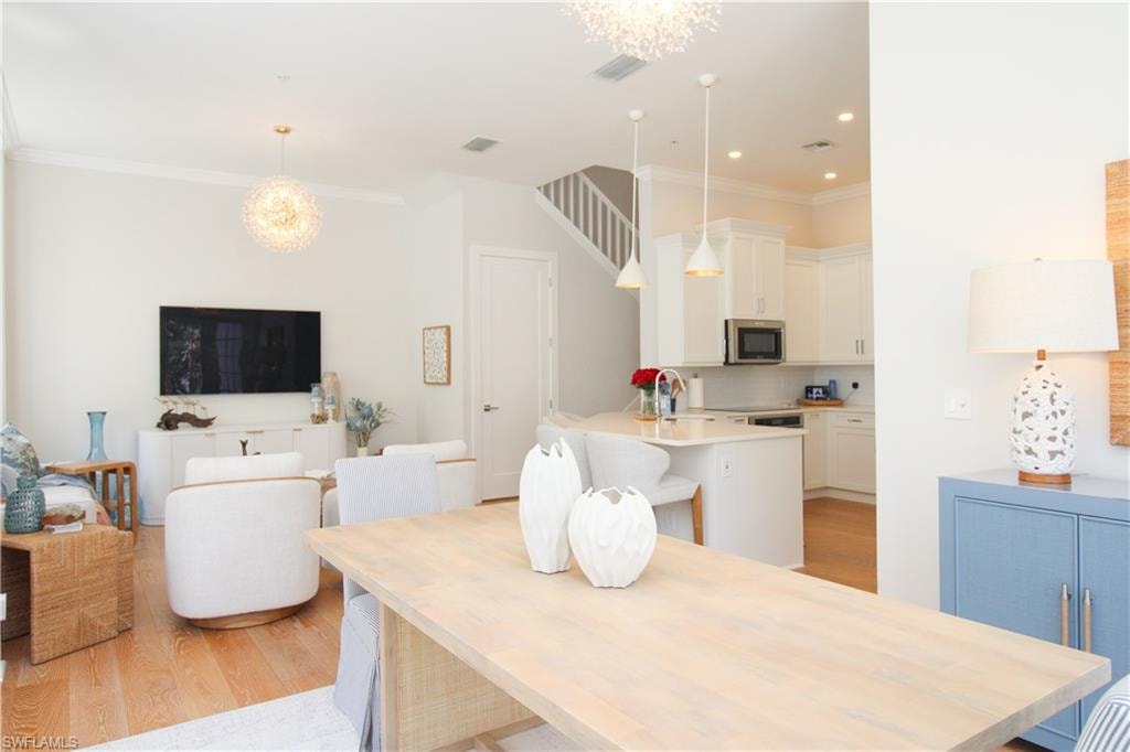 Dining space featuring light wood-type flooring, visible vents, a notable chandelier, and ornamental molding